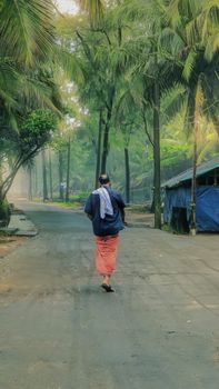 Senior man walking alone on a scenic palm-lined street in Beypore, Kerala.