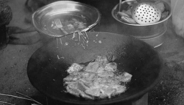 Black and white image of traditional food frying outdoors in a pan.