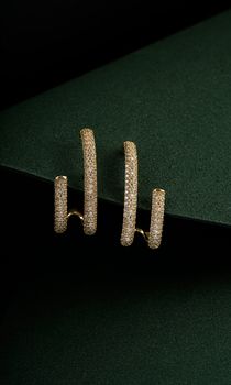 Stylish gold earrings adorned with diamonds on a dark, elegant background.