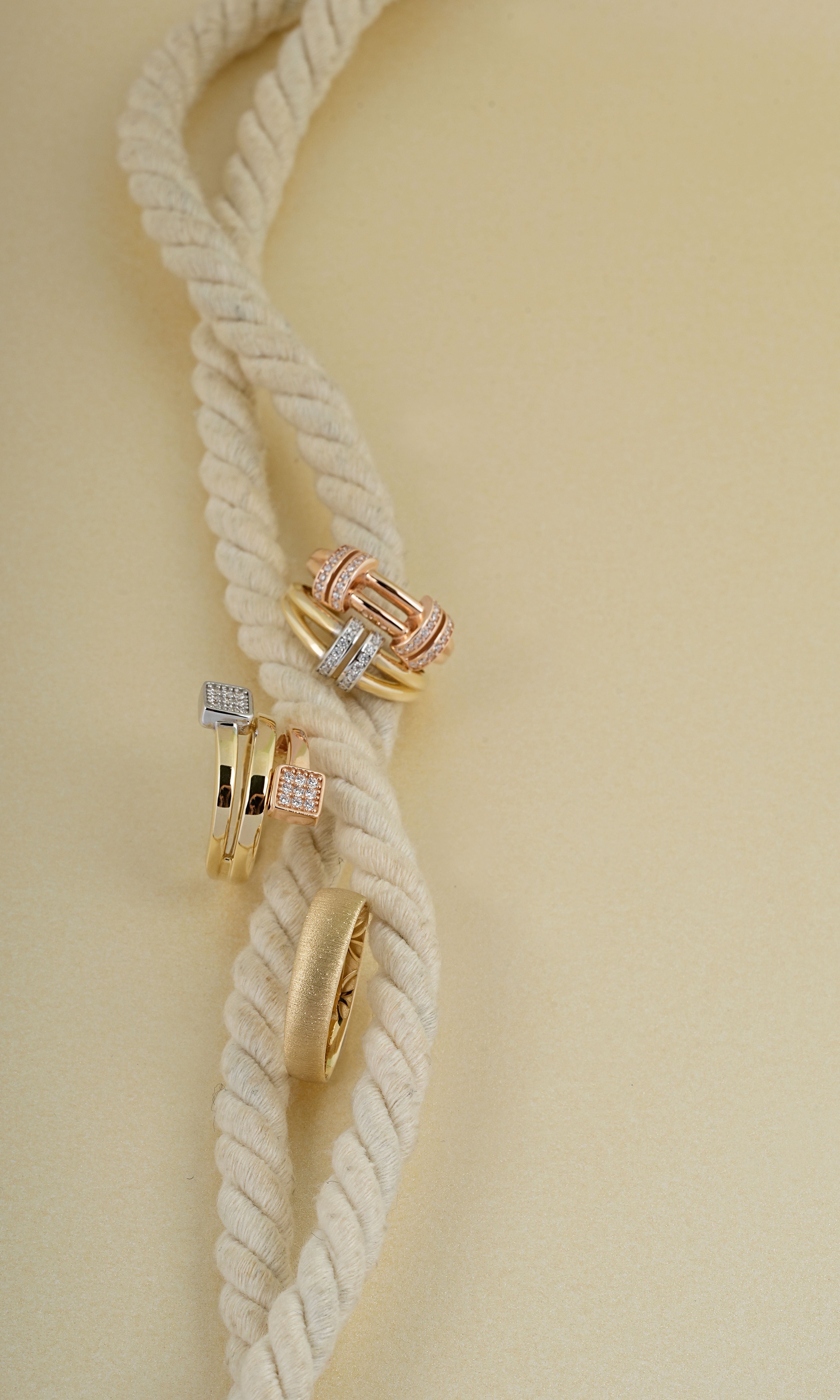 Luxurious gold and diamond rings displayed elegantly on a cream braided rope, creating a sophisticated look.