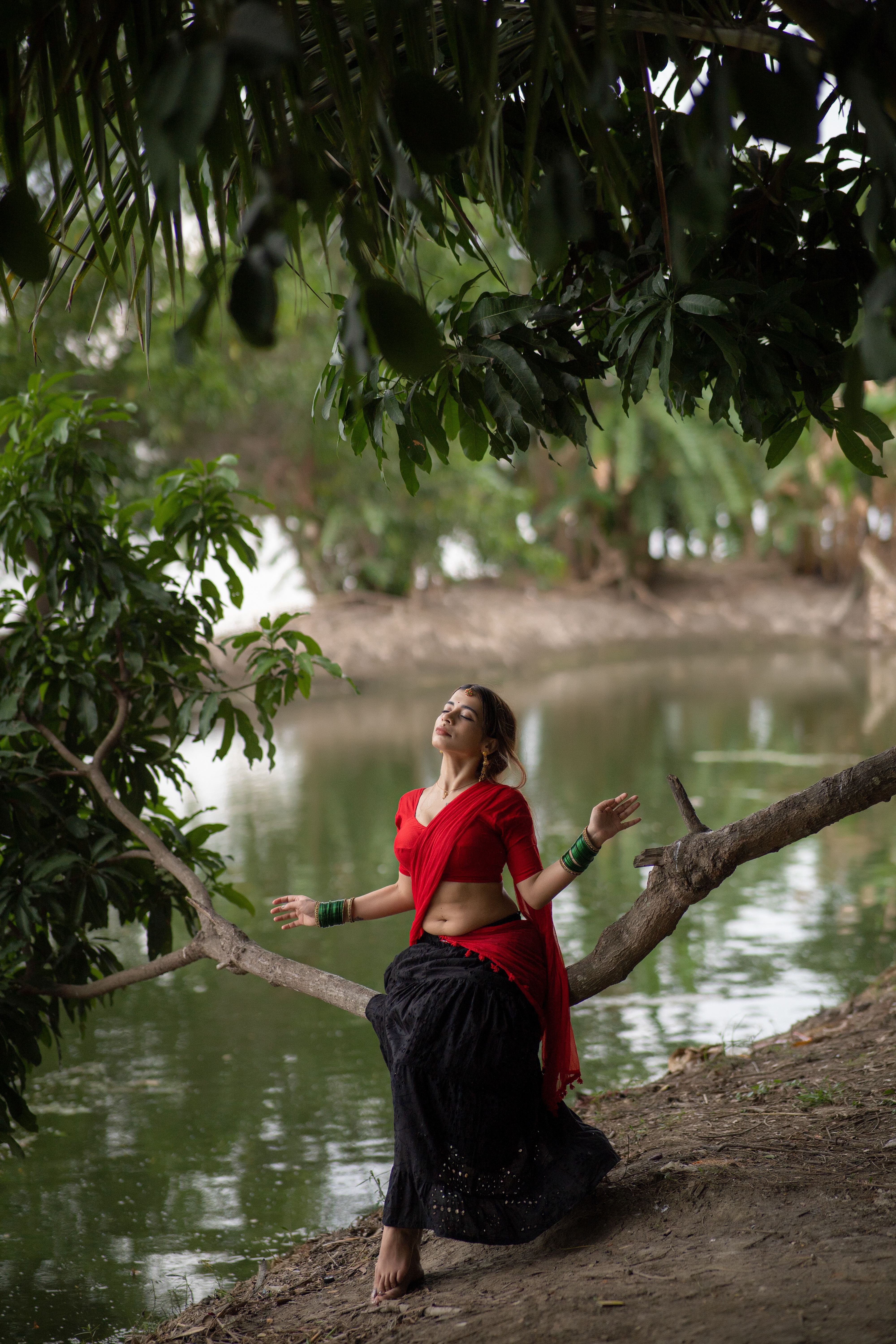 A woman in traditional attire enjoys a peaceful moment by a pond amidst lush greenery.