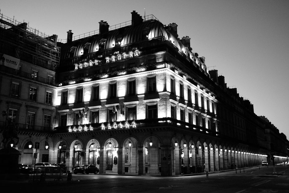 Vista noturna em preto e branco do Hotel Regina, um marco parisiense, transmitindo luxo e profissionalismo para executivos.
