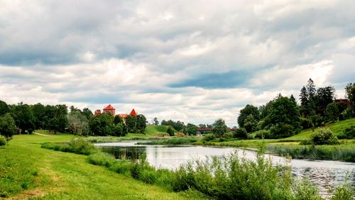 Free Beautiful landscape featuring a castle by a river under a cloudy sky in summer. Stock Photo