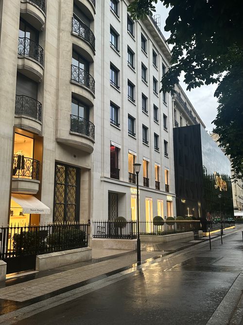 Free Rainy day on a Parisian street featuring luxurious storefronts and elegant architecture. Stock Photo