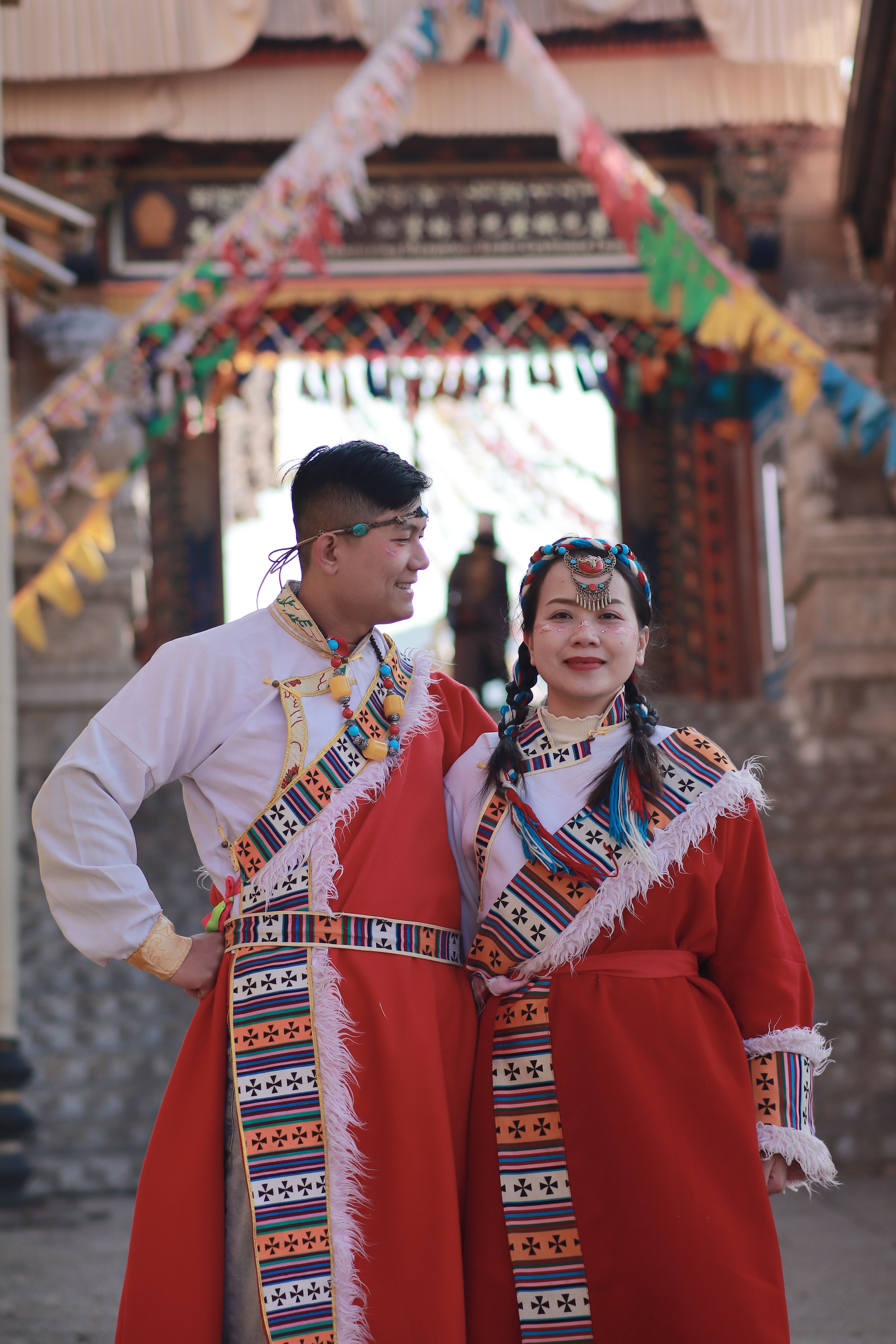 Couple in traditional attire at a colorful outdoor ceremony with festive decorations.