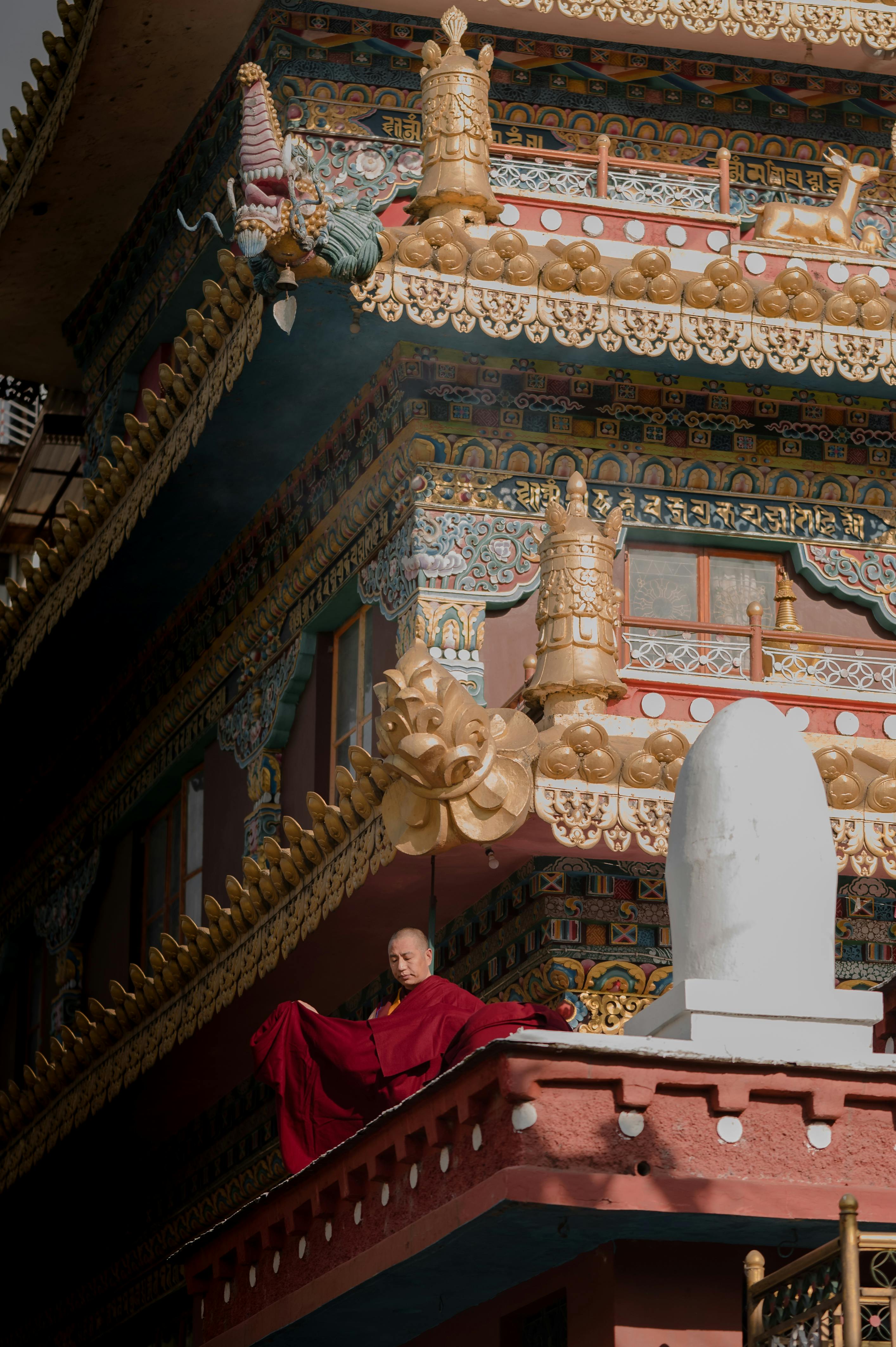 A serene Buddhist monk meditates outside a vibrantly decorated monastery in India.