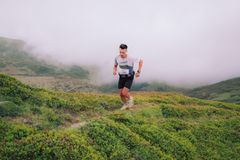A lone runner ascends a vibrant green hill enveloped in fog, creating a serene outdoor scene.