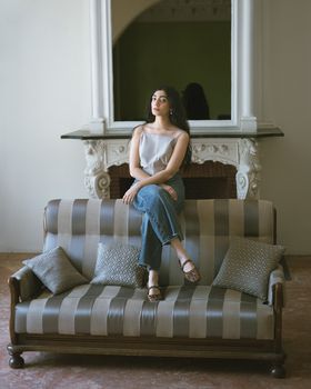 Contemplative woman sitting on stylish sofa indoors. Casual and elegant.