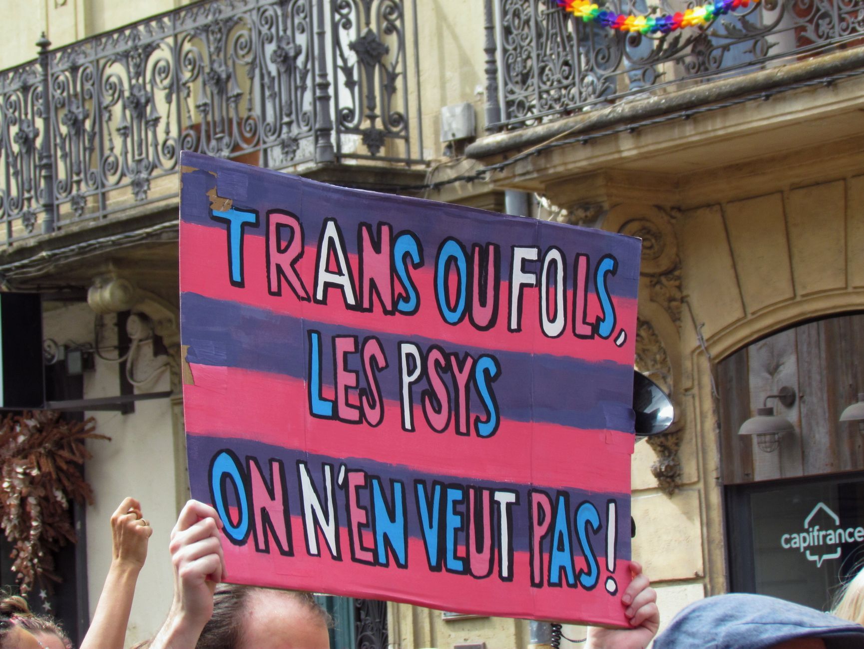 Manifestante erguendo um cartaz com as cores trans e bi durante um desfile LGBT+ na cidade