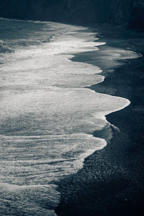 Free A stunning view of Iceland's black sand beach with dramatic ocean waves and rugged coast. Stock Photo
