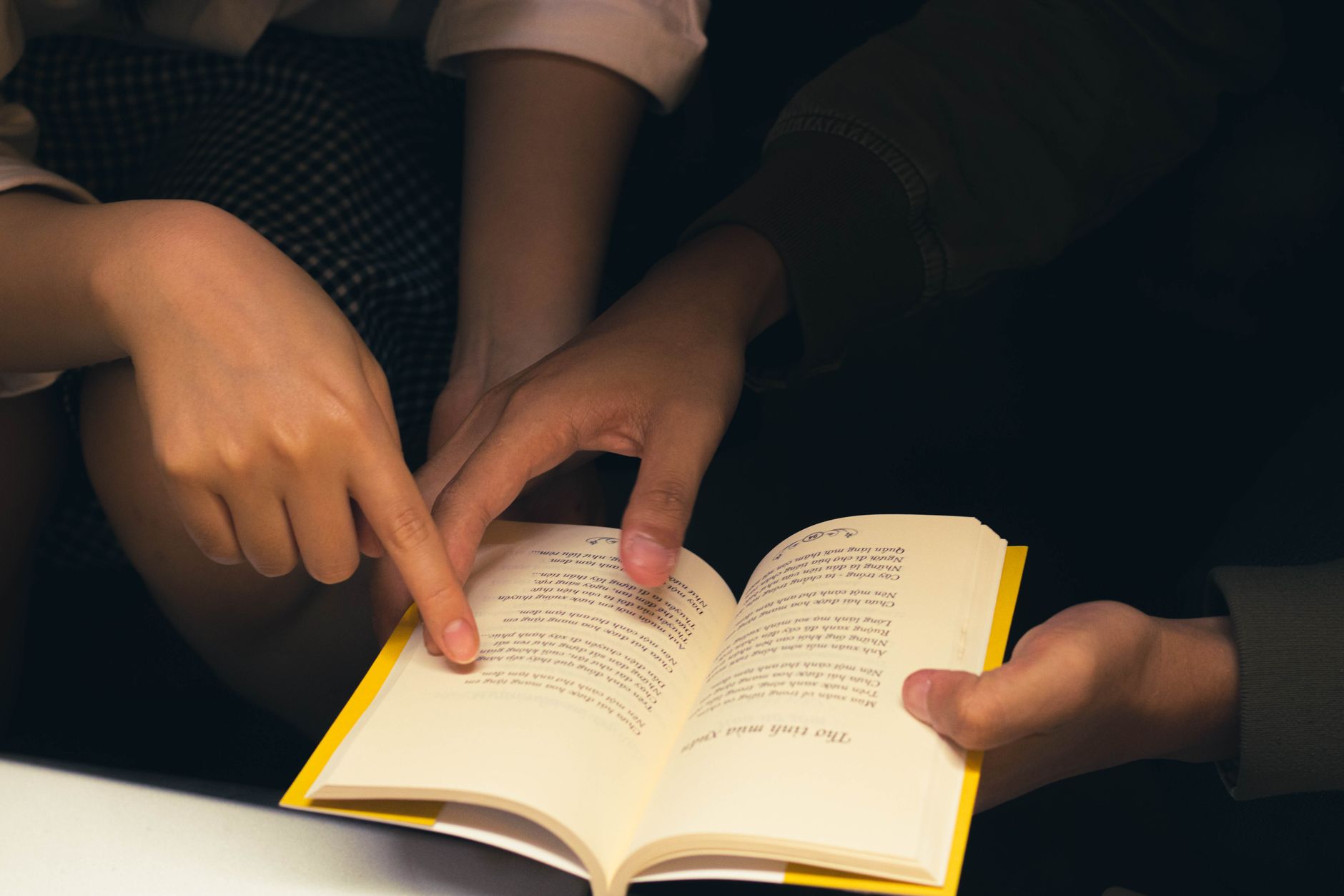 Close-up of two people sharing a book, pointing at text, creating a cozy reading atmosphere.