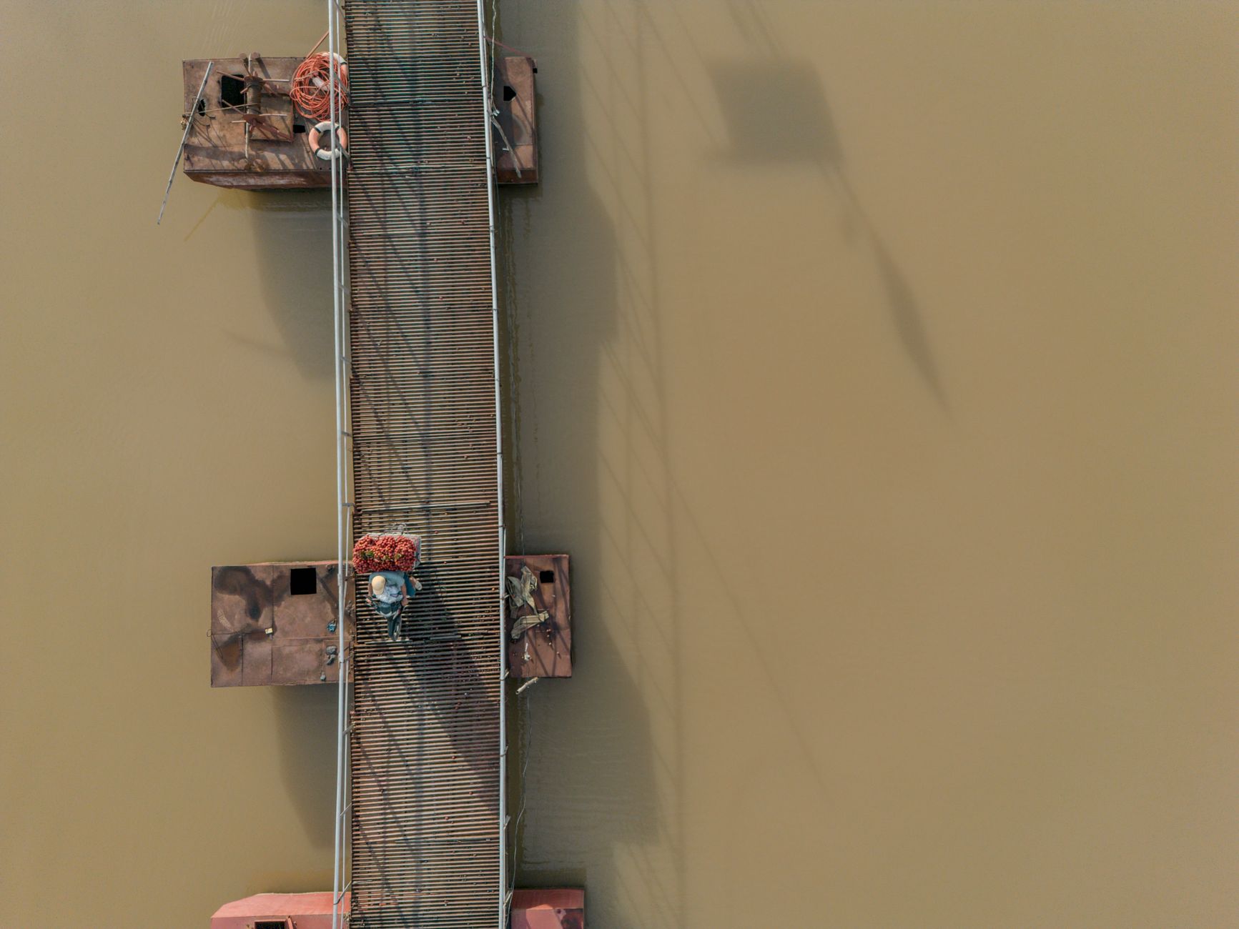 Aerial view of a wooden bridge over a river in Bac Giang, Vietnam, with a person carrying lychees.