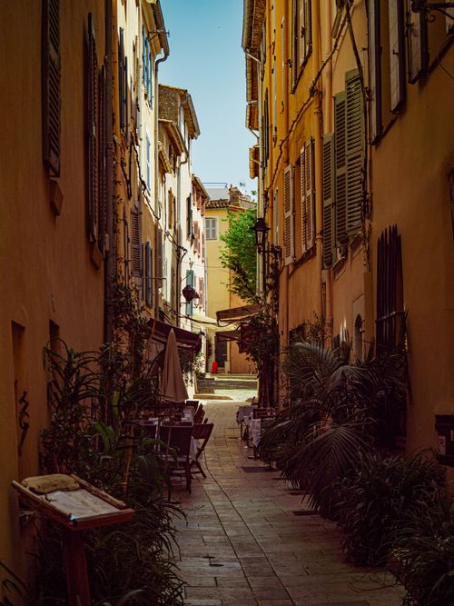 Free Explore a quaint Mediterranean alley with charming outdoor café seating, bathed in warm sunlight. Stock Photo
