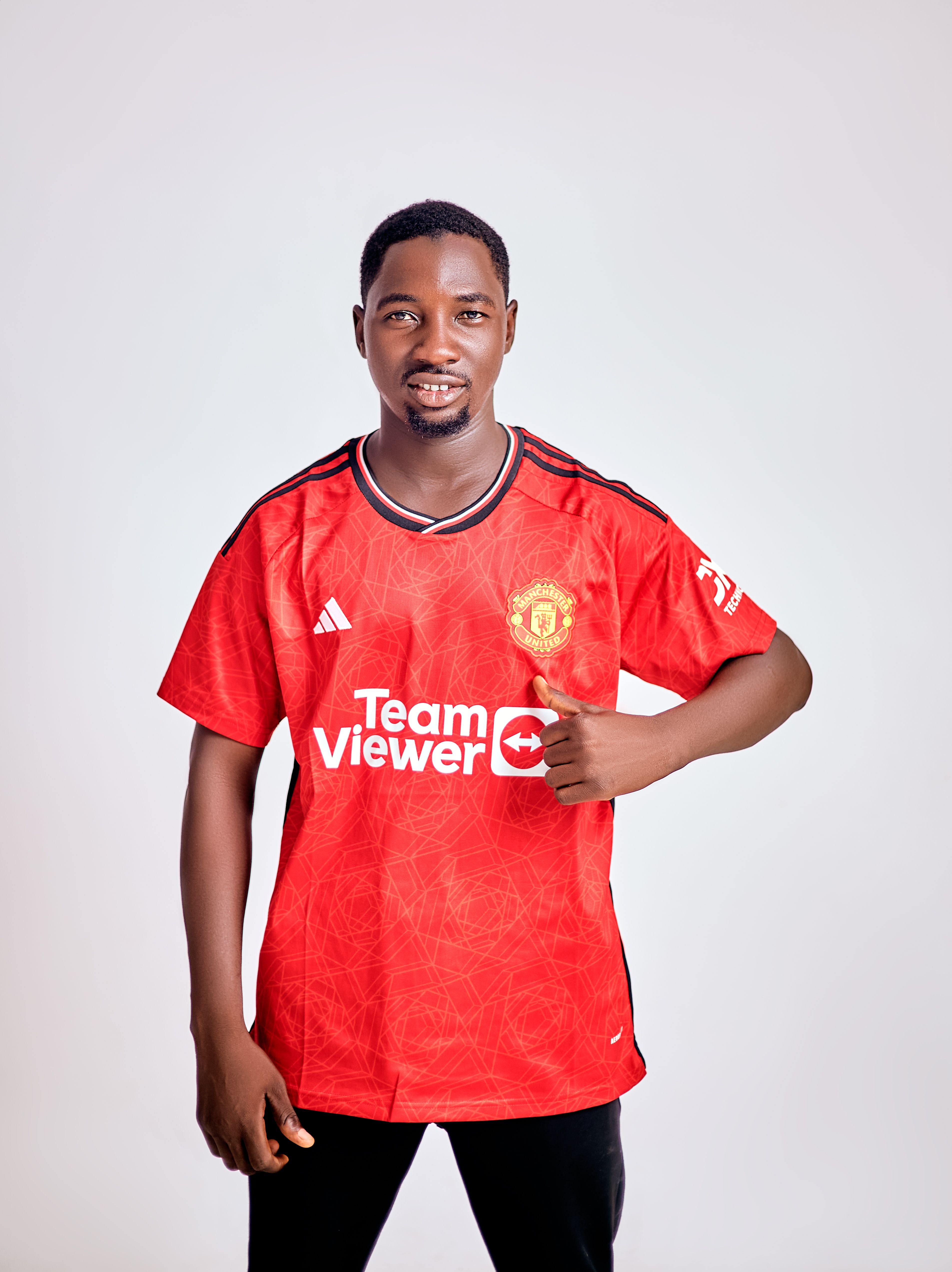 Man in a red soccer jersey giving a thumbs up, posing cheerfully indoors.