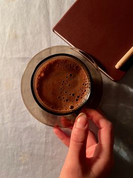 Top view of a coffee cup in hand beside a notebook, perfect for a cozy workspace scene.
