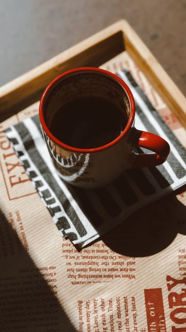 A cozy red coffee mug on a sunlit table creates a warm morning ambiance.