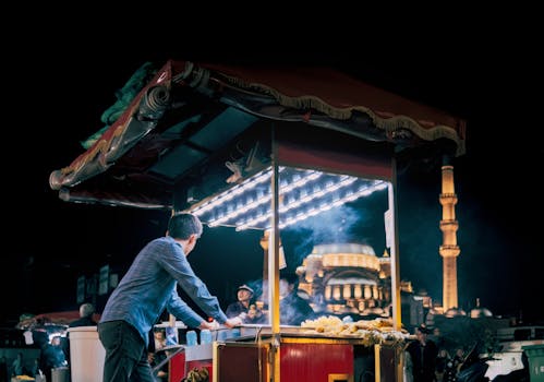 Explore the lively night scene at a street food stall in Istanbul, with a majestic mosque in the background.