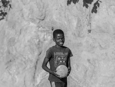 Black and white photo of a young boy holding a soccer ball, outdoors.