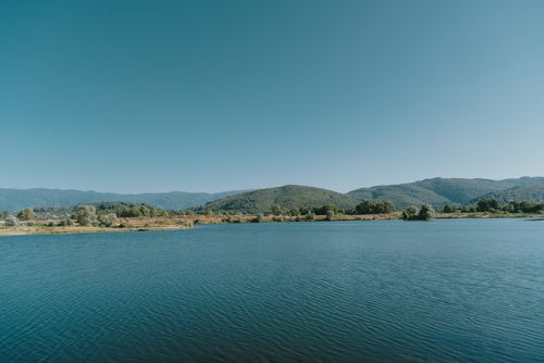Free Peaceful outdoor scene of a lake with lush mountains under clear blue sky. Stock Photo
