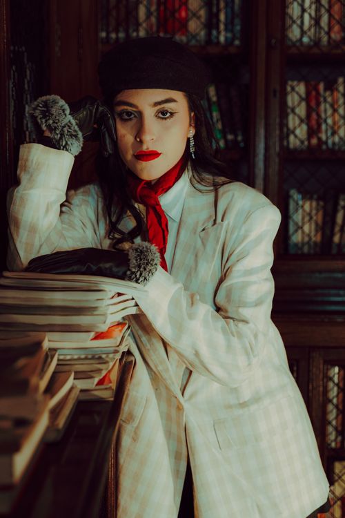 Free Elegant woman in winter attire leaning on a library bookshelf, exuding vintage charm. Stock Photo