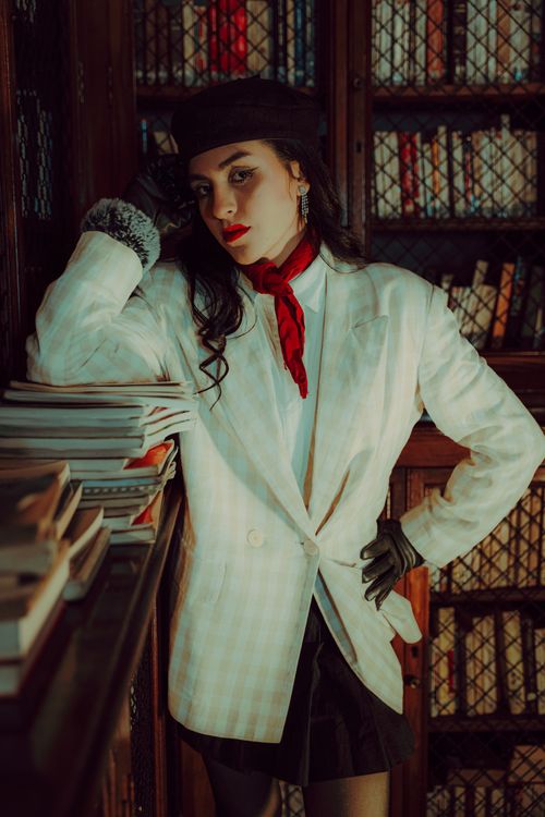 Free Elegant woman in library with chic outfit, red scarf, and beret, exuding vintage charm. Stock Photo