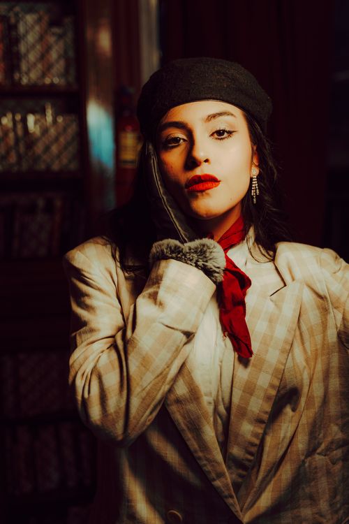 Free Portrait of a woman in vintage attire with a red scarf and hat in a cozy setting. Stock Photo
