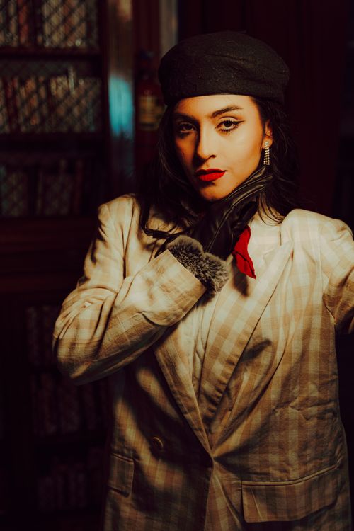 Free Stylish woman wearing a black beret and checkered suit poses thoughtfully indoors in warm lighting. Stock Photo