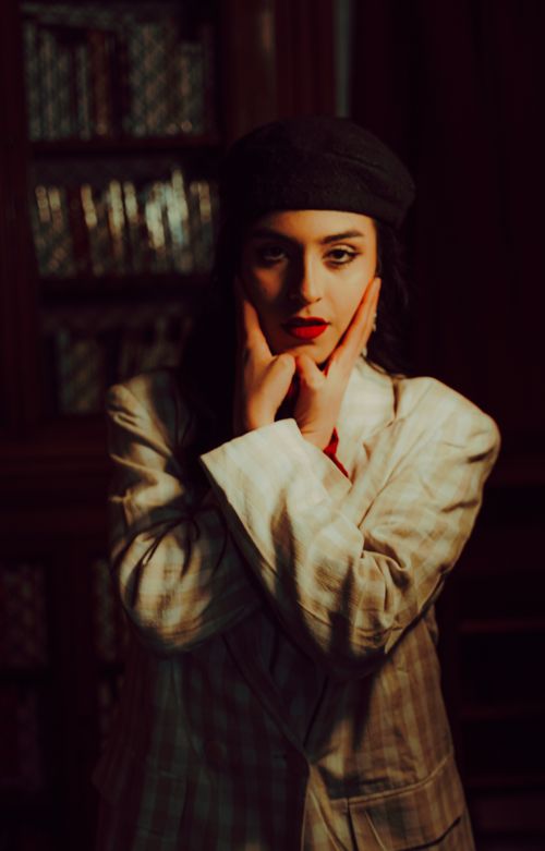 Free Artistic portrait of a woman in a retro outfit posing indoors against a bookshelf background. Stock Photo