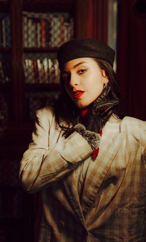 Free Elegant woman wearing a vintage checkered suit and beret in a classic library setting. Stock Photo