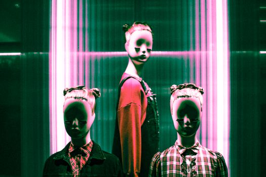 Stylish mannequins in a dark, neon-lit fashion display create an eerie and surreal ambiance.