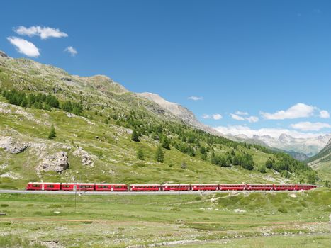 Experience the breathtaking view of a red train traversing the picturesque Bernina Pass in Switzerland's Alps.