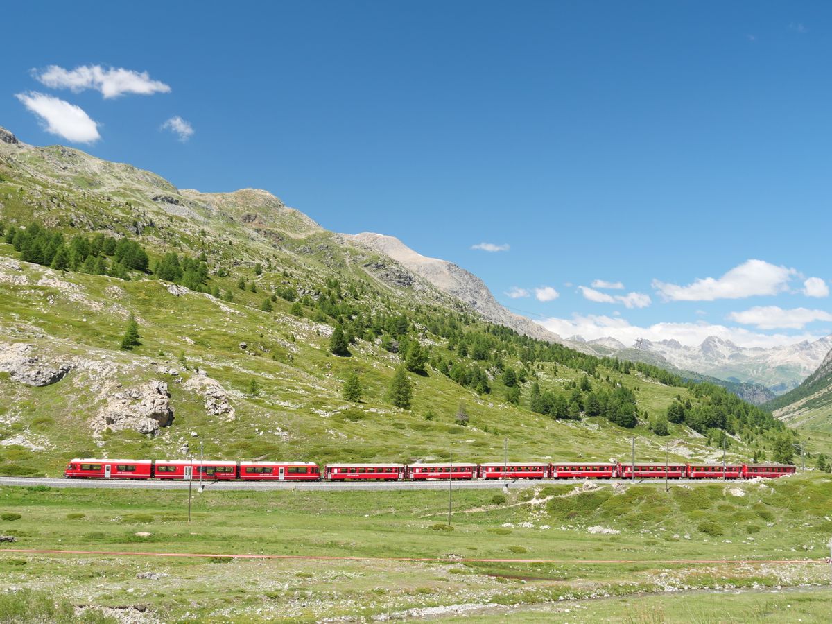 A red train travels through the Bernina Pass landscape in the Swiss Alps