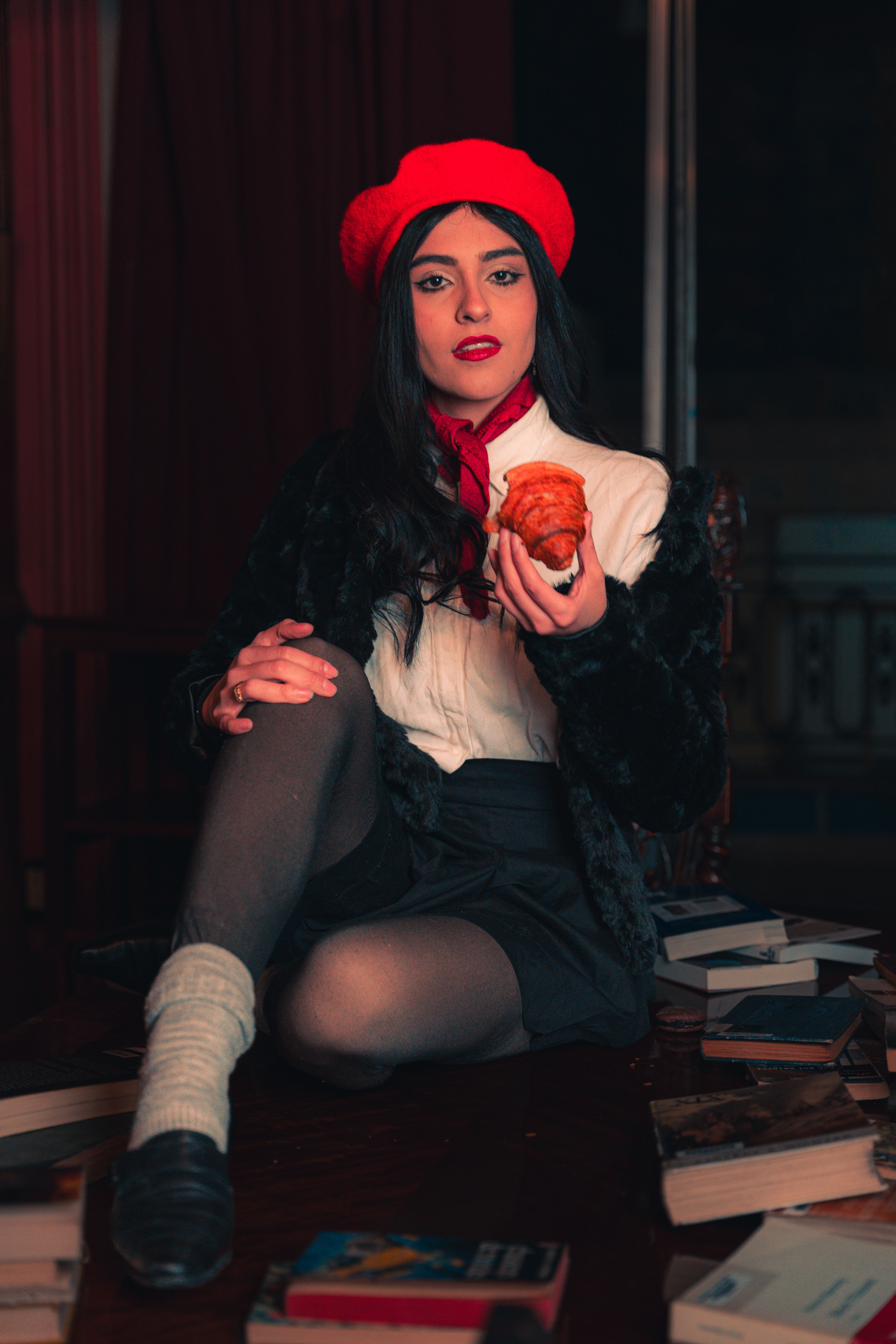 Fashionable woman in a red beret enjoying a croissant indoors. Elegant and sophisticated look.