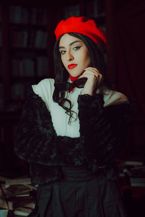 Free Stylish woman in a black fur coat and red beret poses confidently in a cozy library. Stock Photo