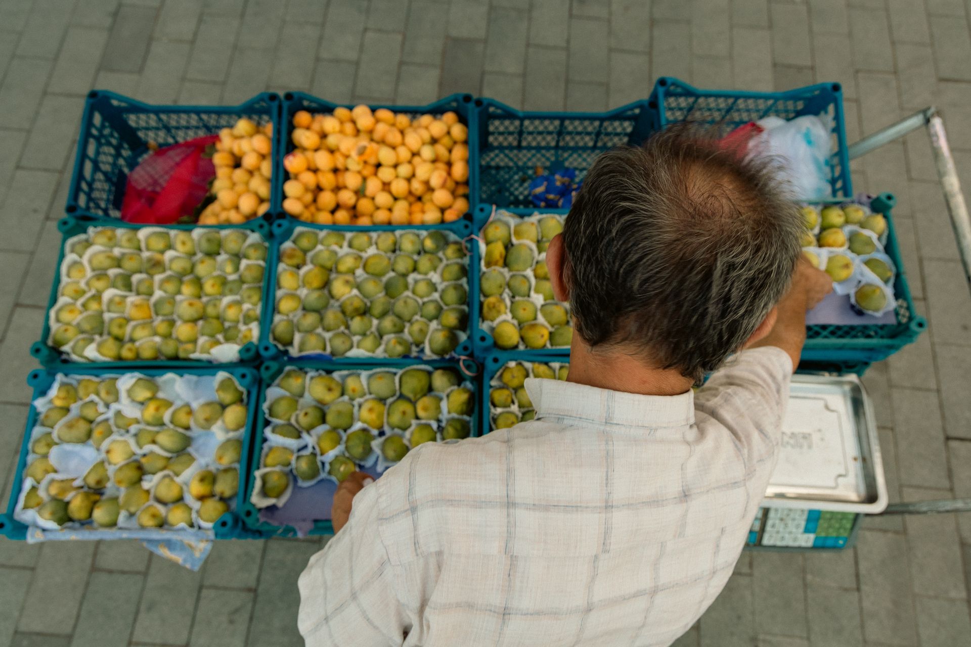 Overhead view of a fruit seller arranging figs and apricots in Bursa's bustling market.