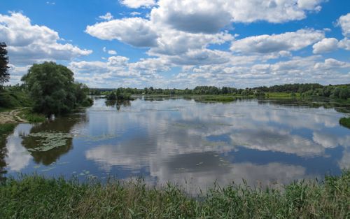 Free Tranquil summer lake surrounded by nature in Kharkiv, Ukraine, reflecting a blue sky and white clouds. Stock Photo
