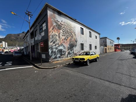 A vintage yellow car parked next to a stunning leopard mural in Cape Town's Salt River district.