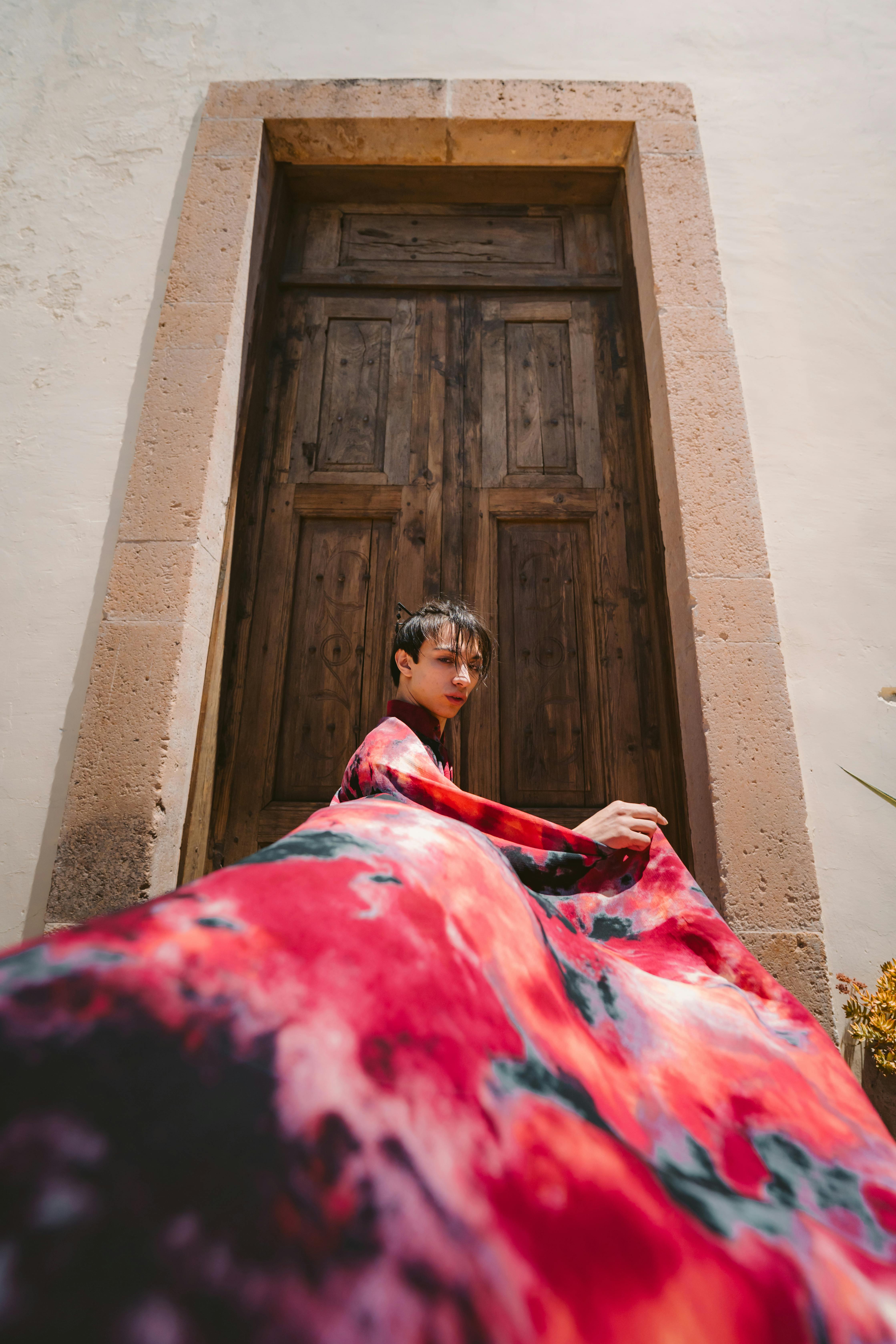 A person in colorful attire poses dramatically before a rustic wooden door in León, México.
