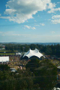 Aerial shot of an outdoor festival with a distinctive white tent under a bright sky.