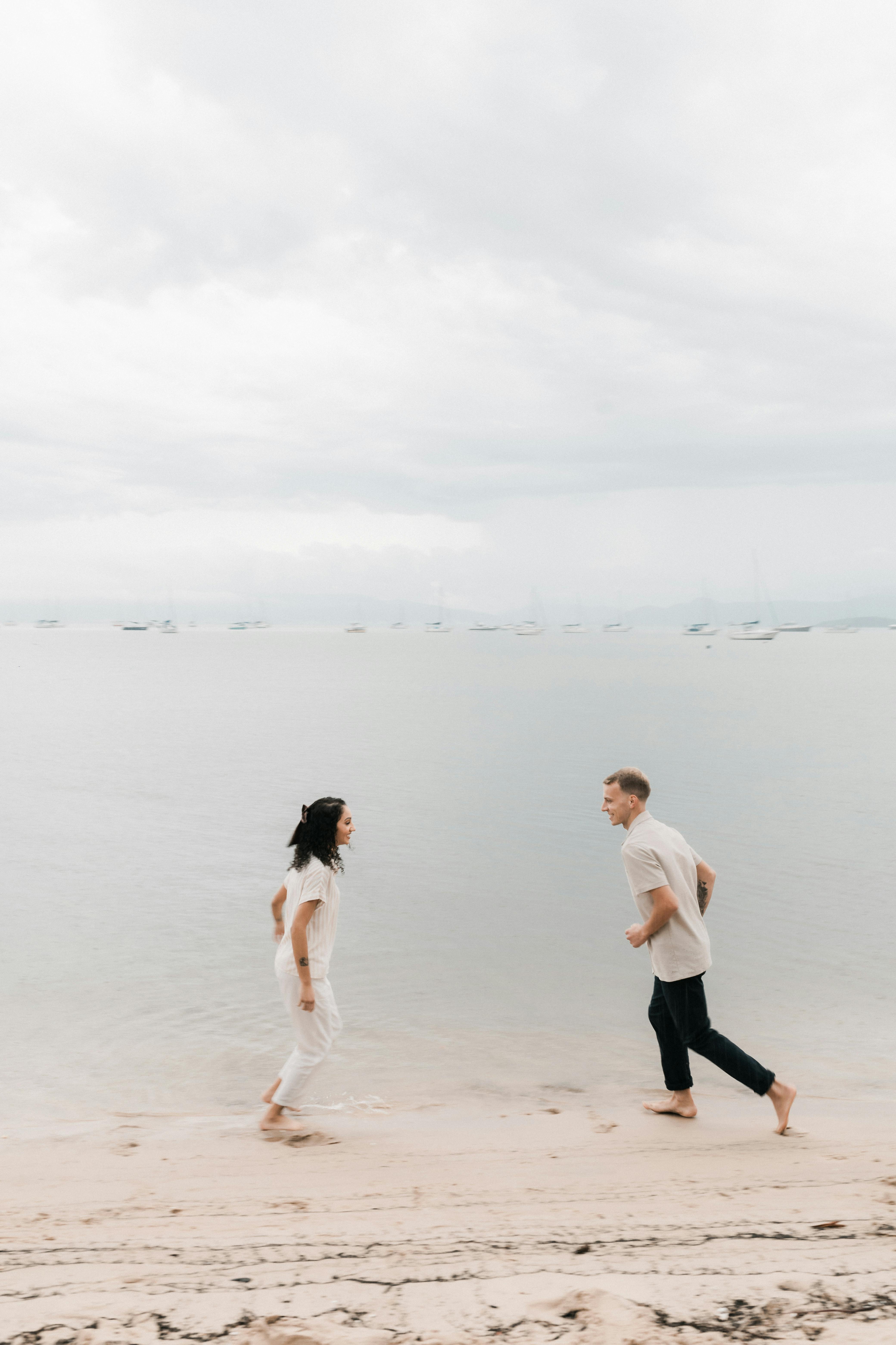A couple joyfully running on a serene beach, capturing a moment of happiness and freedom.