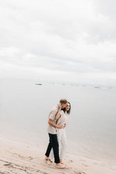 A couple enjoying a peaceful walk on a sandy beach under a cloudy sky, embracing love and tranquility.