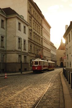 Vintage tram on cobblestone street with historic buildings at sunset. European charm.