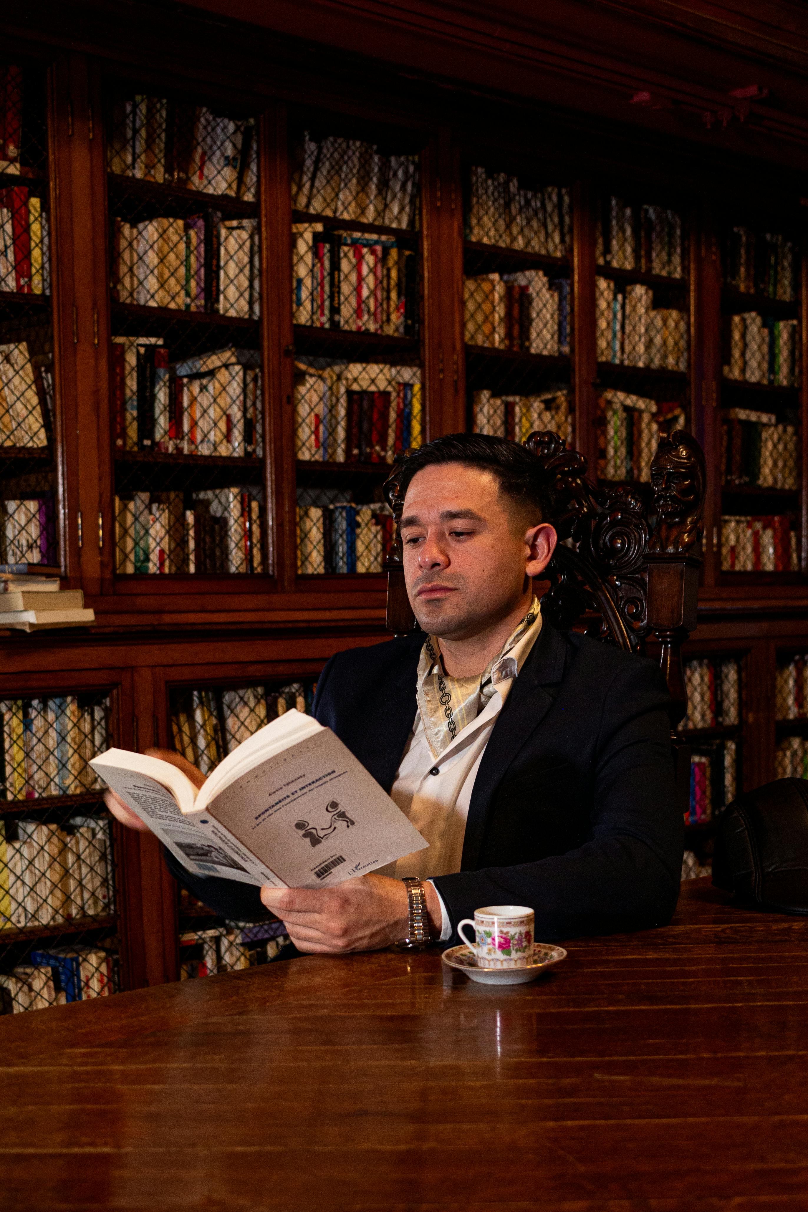 Gratis Un uomo legge un libro in un'elegante biblioteca rivestita in legno. Foto a disposizione