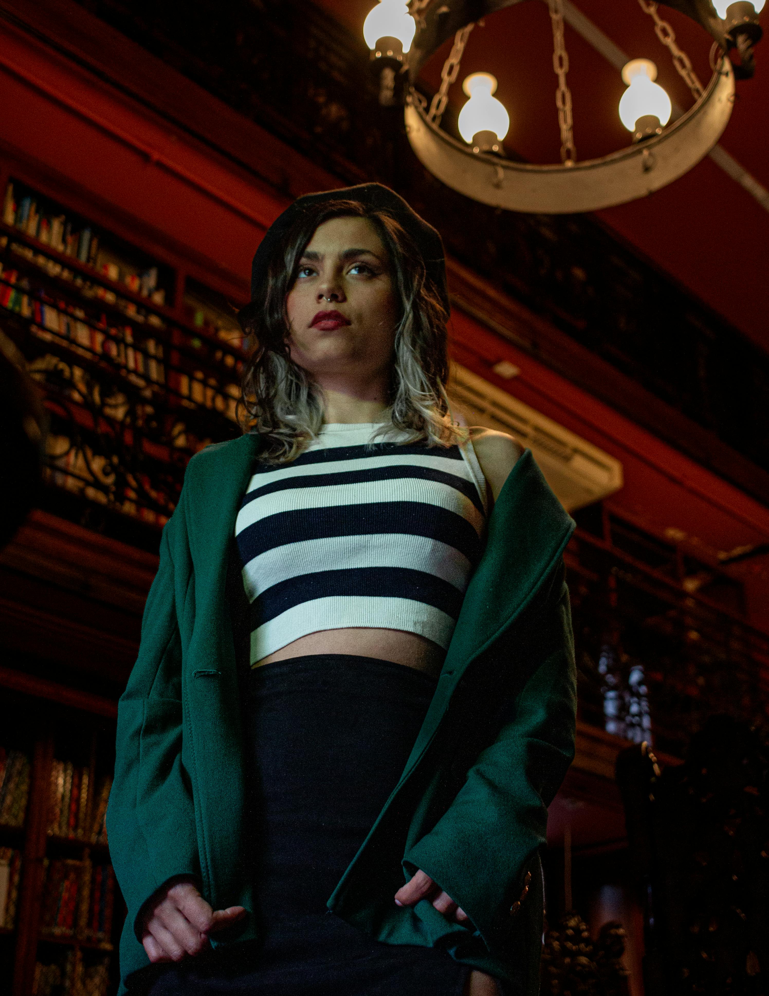 Free Stylish woman in a library wearing a striped top and green blazer, exuding confidence and elegance. Stock Photo