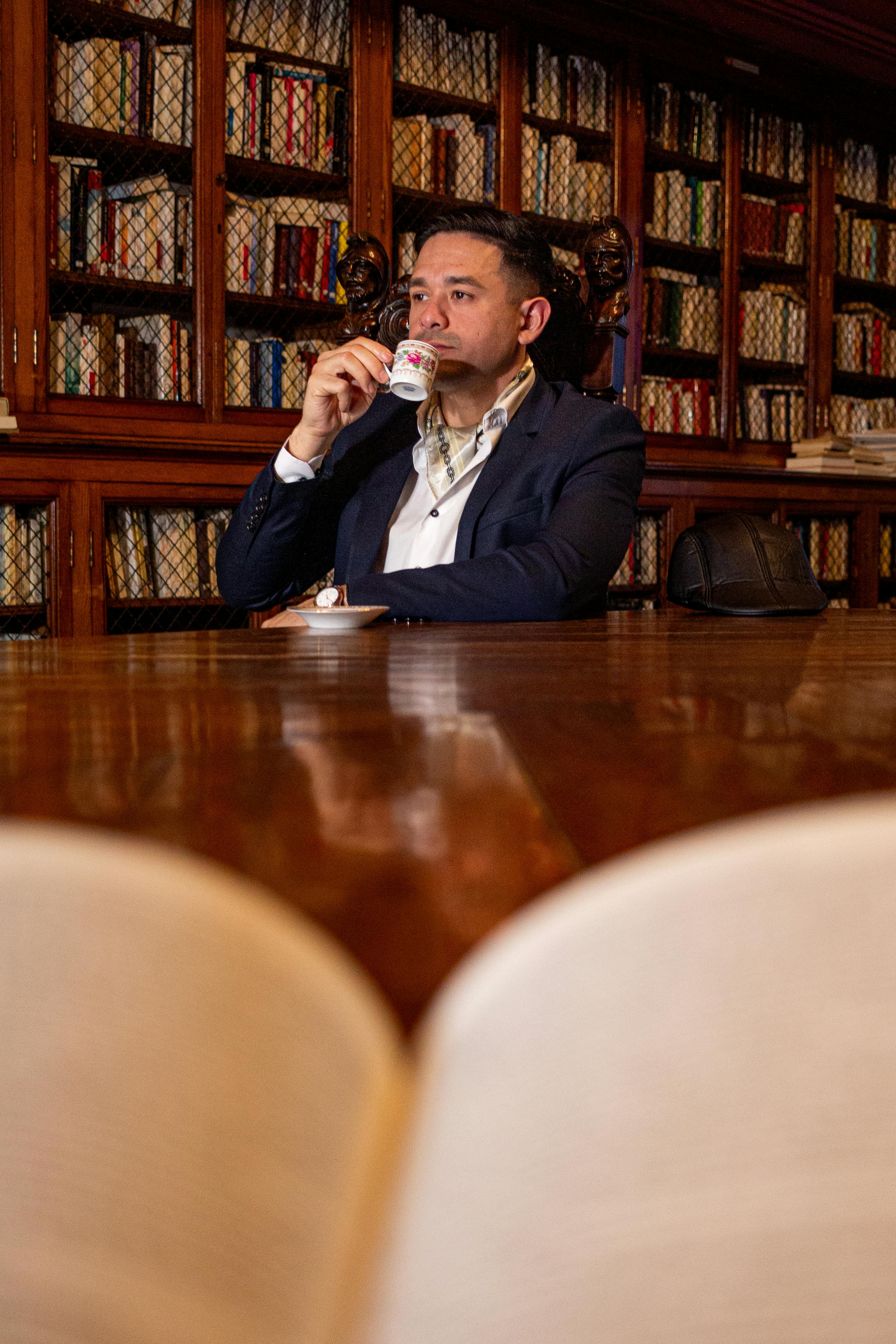 Kostnadsfria Man njuter av kaffe i en klassisk biblioteksmiljö i Buenos Aires, omgiven av böcker. Stock foto