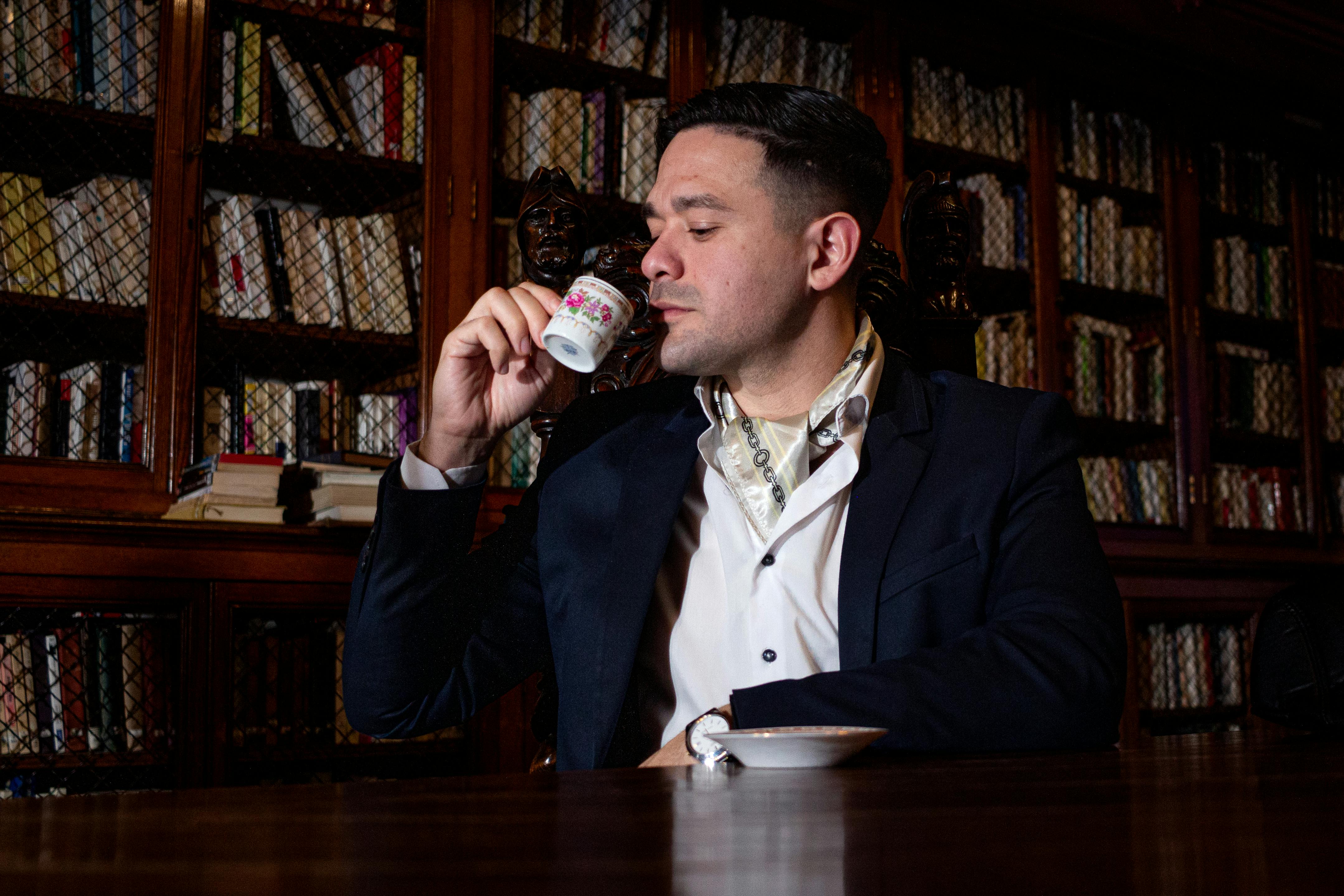 bezplatná Stylový muž si pochutnává na espressu v zdobeném prostředí knihovny a vyzařuje eleganci. Základová fotografie