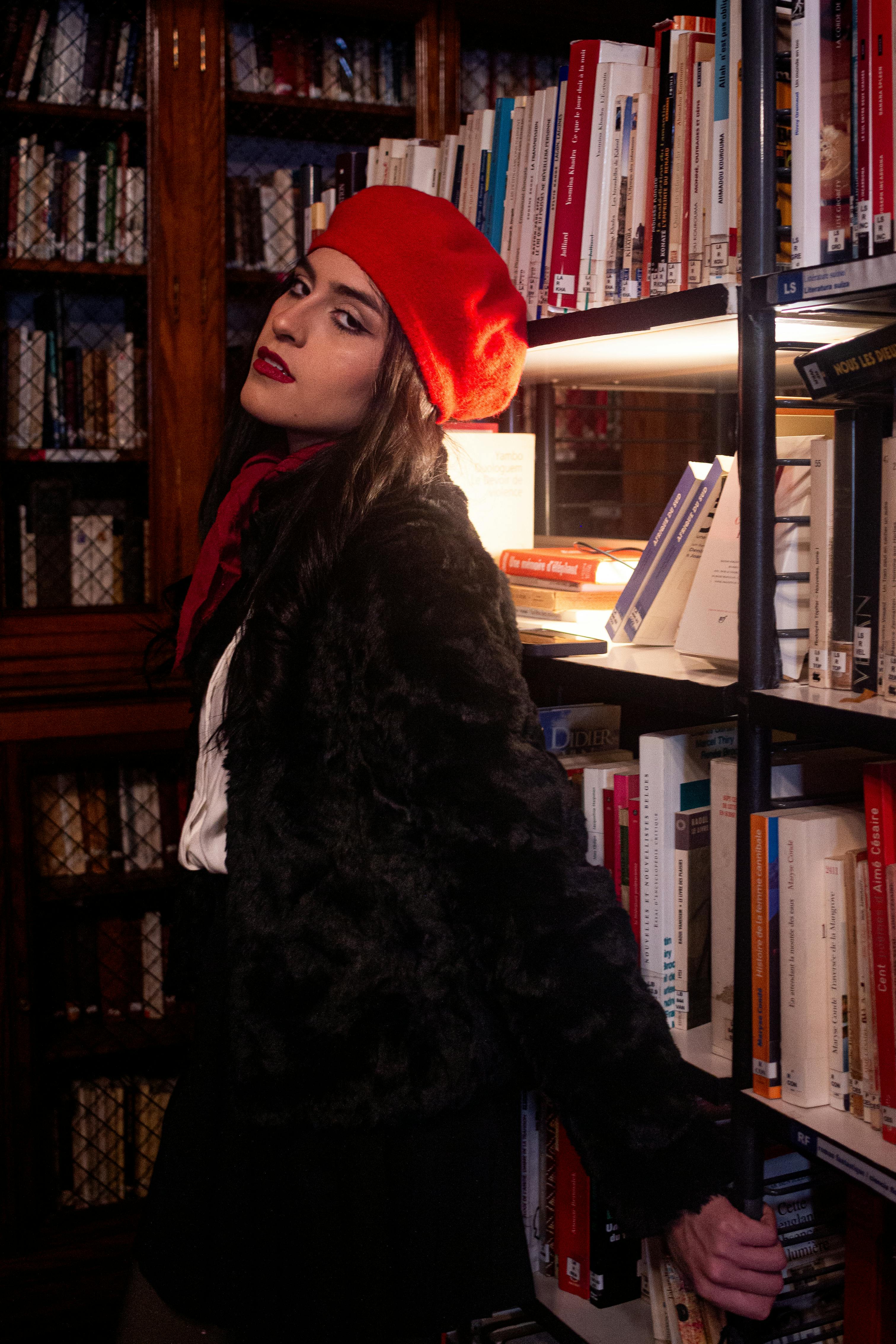 Gratis Una donna alla moda con un basco rosso posa contro gli scaffali di una biblioteca di Buenos Aires. Foto a disposizione