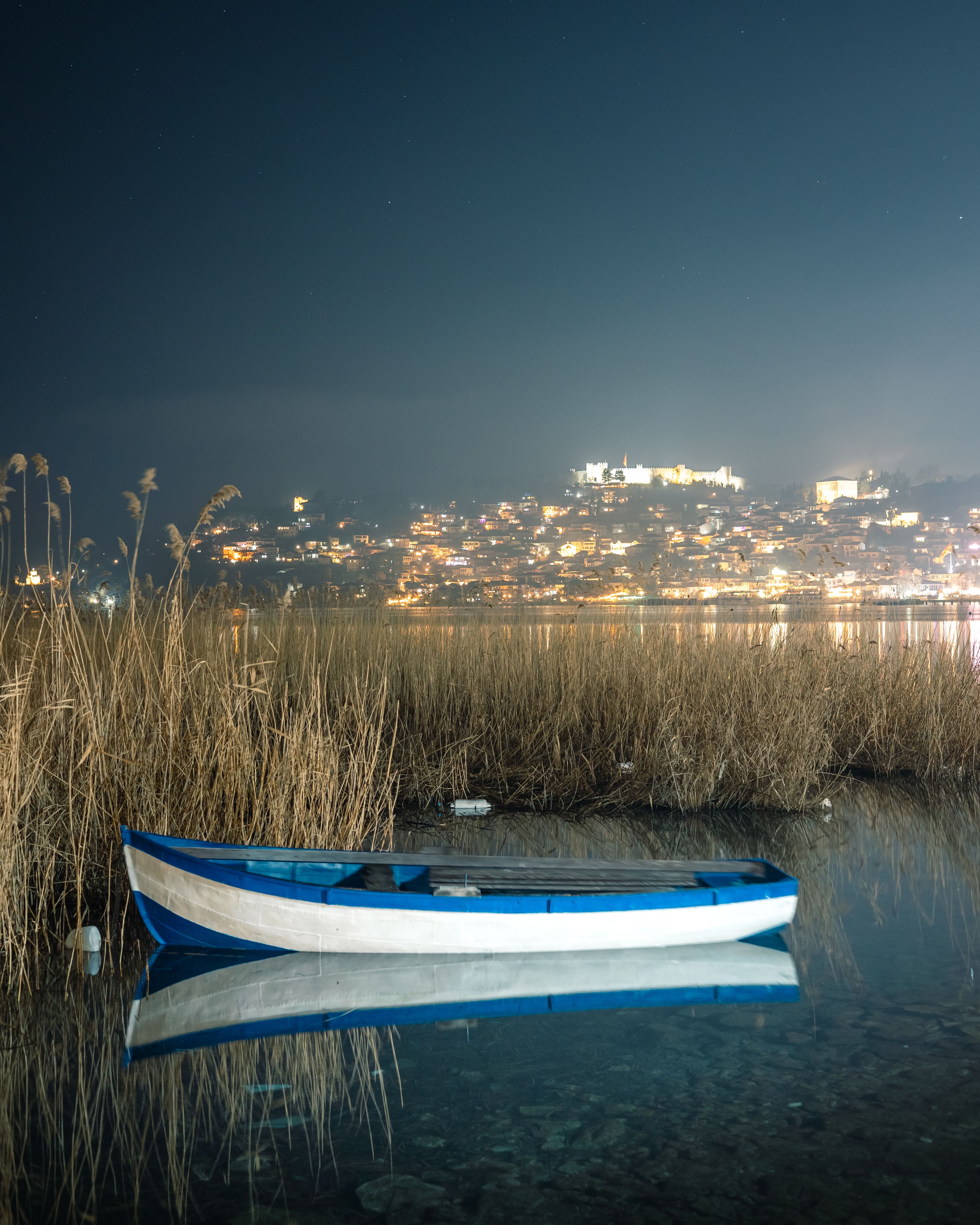 Serene nightscape of Ohrid, North Macedonia, featuring a calm lake with boat reflection.