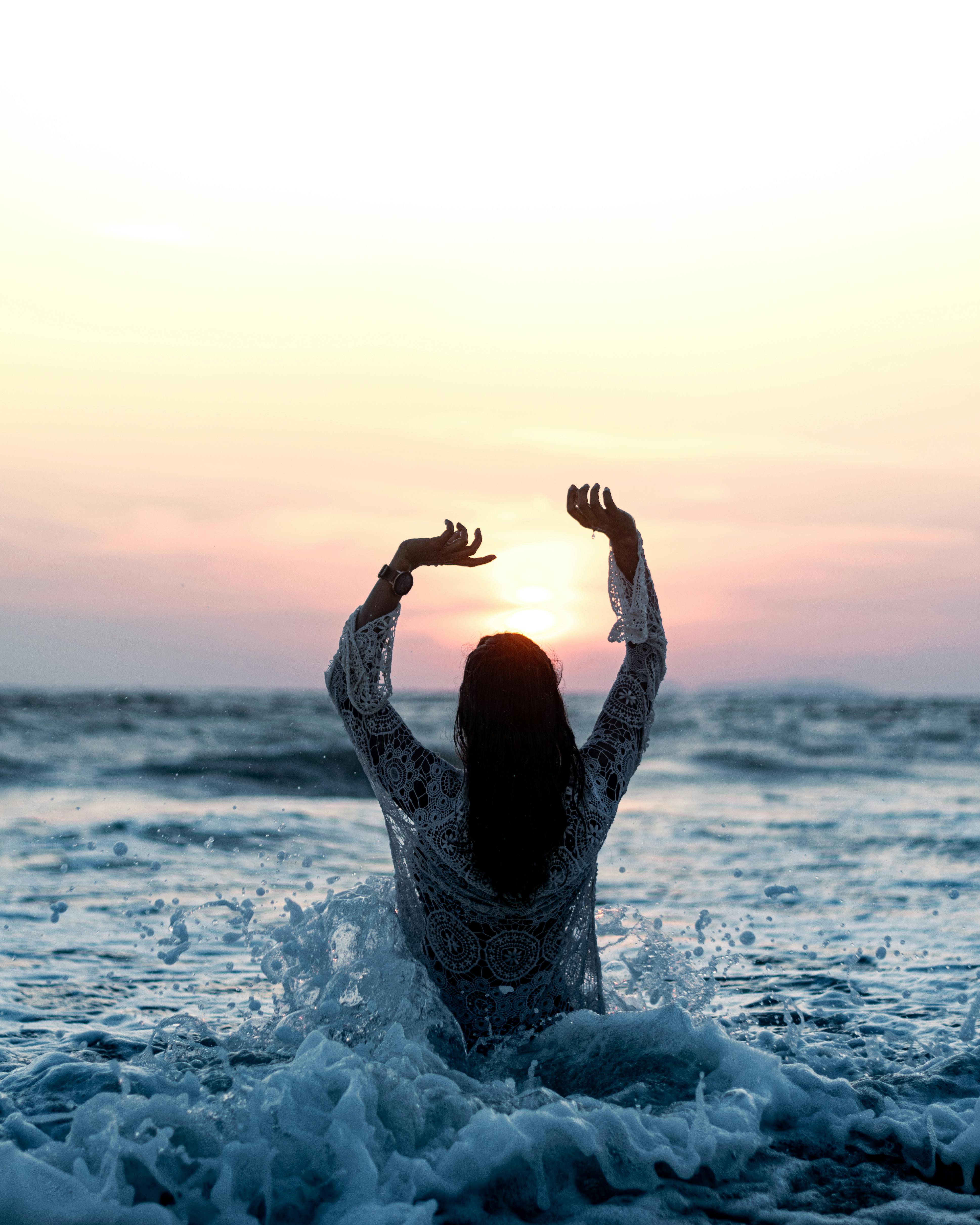 An adult woman joyfully interacting with ocean waves during a scenic sunset.