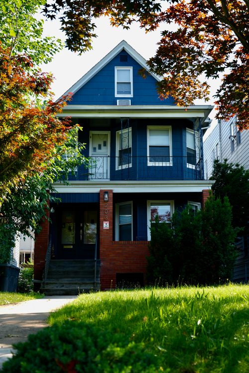 Free A beautiful blue and red brick suburban house framed by trees on a sunny day in New Jersey. Stock Photo